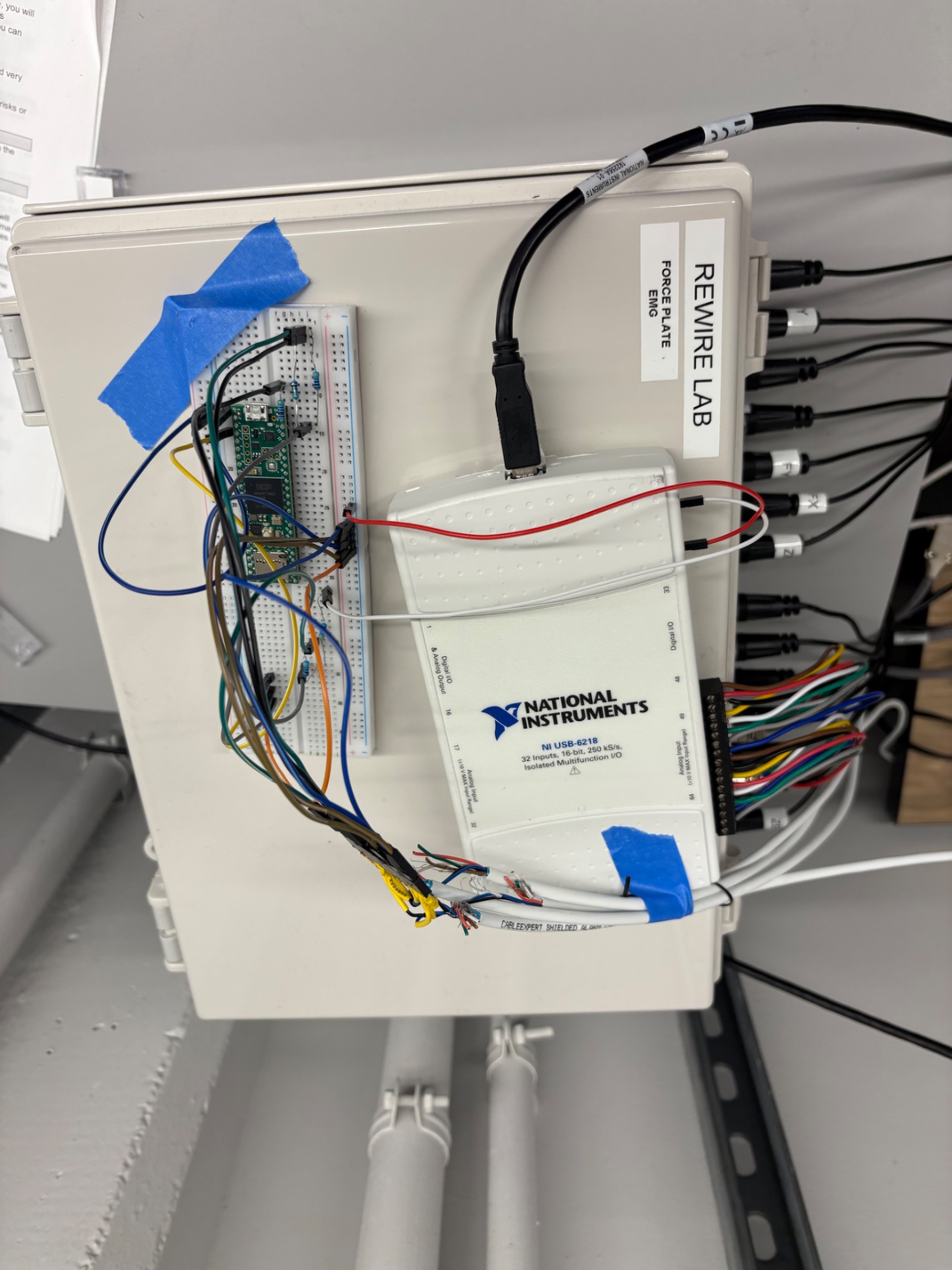 Bench wiring showing the NI USB-6218 DAQ, breadboard with Teensy, and force plate/EMG input cables at the HeRo Lab